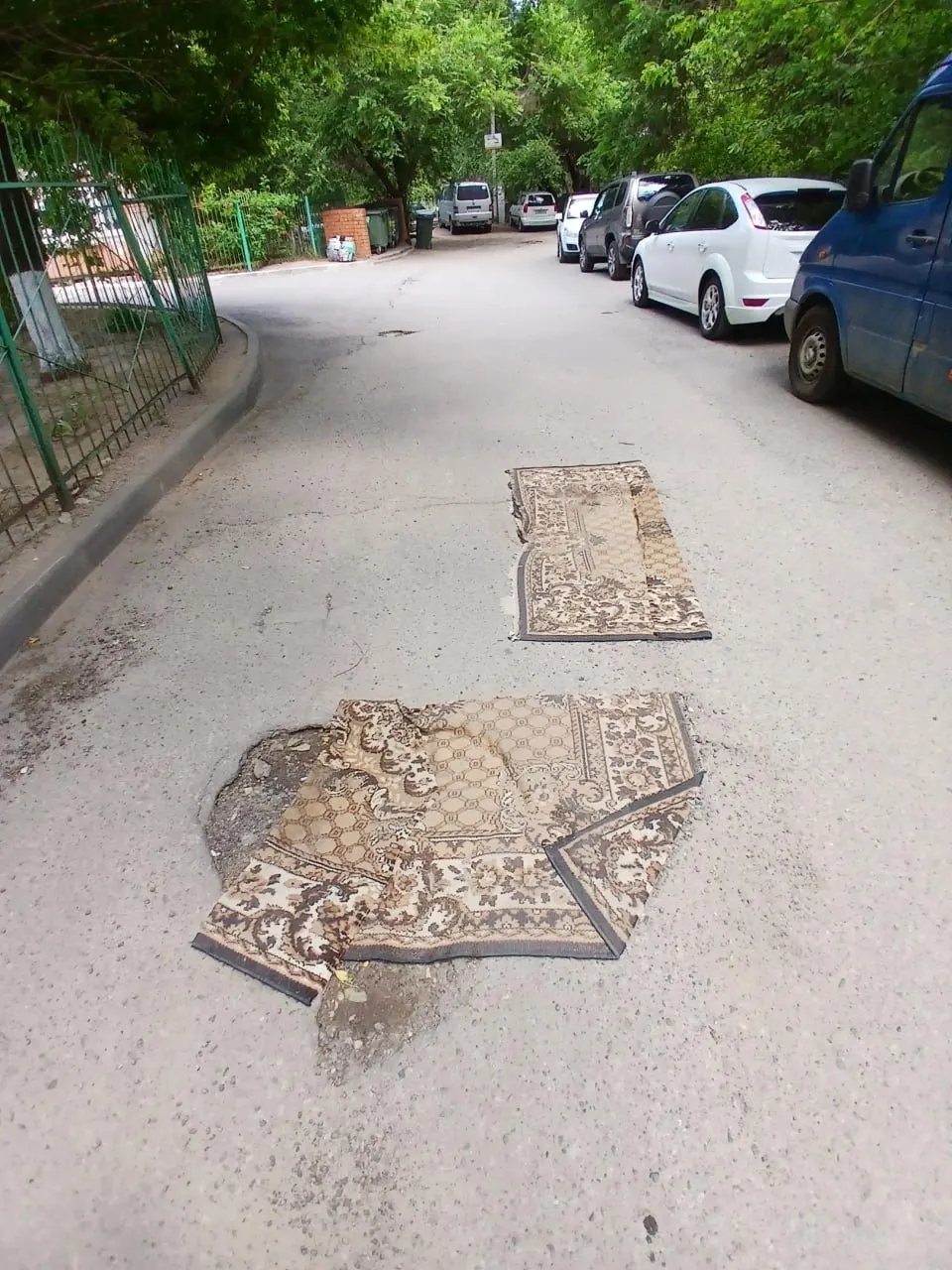 В Дзержинском районе местные жители временно накрыли дорожные ямы коврами — короткая мера до приезда дорожников.